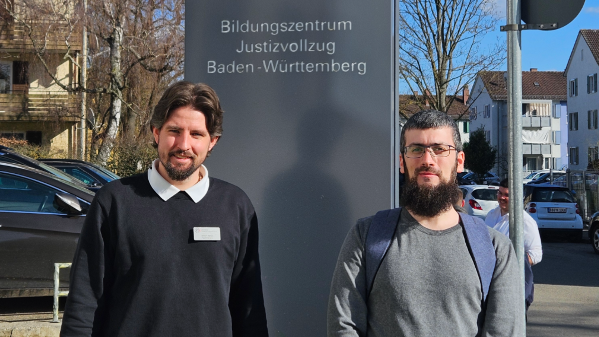Zwei Männer stehen vor einem Schild mit der Aufschrift Bildungszentrum Justizvollzug Baden-Württemberg